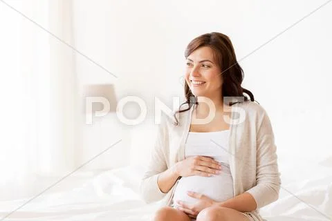 Happy pregnant woman sitting on bed at home Stock Photos