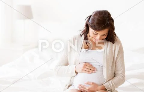 Happy pregnant woman sitting on bed at home Stock Photos