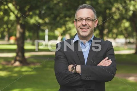 Happy professor looking at camera with arms folded on campus Stock Photos