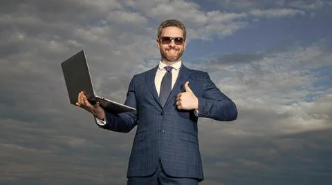 Happy programmer holding laptop. Computer programmer showing thumb gesture 스톡 사진