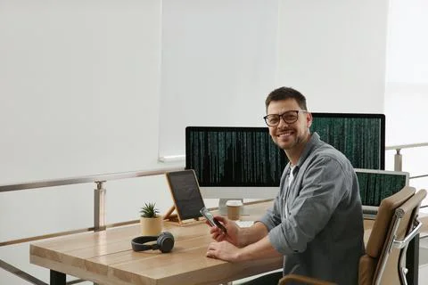 Happy programmer with smartphone working at desk in office 写真素材