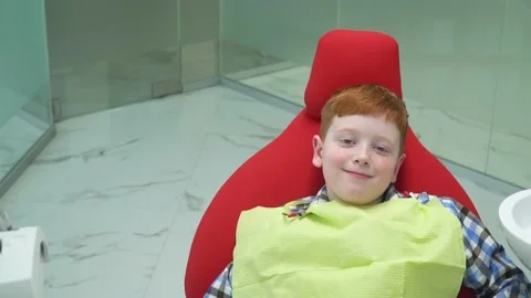 Happy red-haired boy at reception at dentist in dental chair that rises. Safe Stock Footage 131228874
