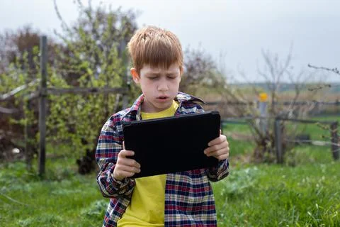 Happy redhead boy playing tablet or watching cartoons, walking in the backyar Stock Photos