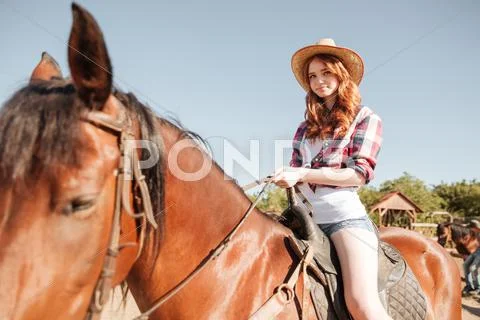Happy redhead young woman cowgirl smiling and riding horse Stock Photos
