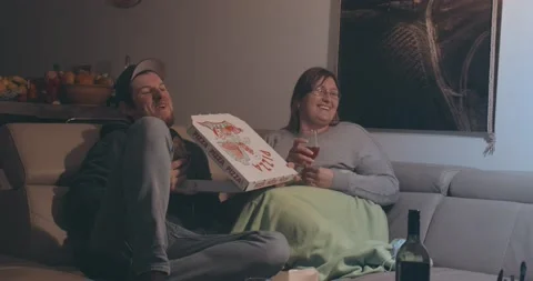 Happy Relaxed Couple Sit On Sofa and Watch Together Movie On Tv And Eating Pizza Stock Footage 144924161