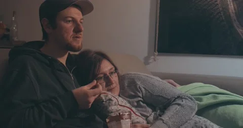Happy Relaxed Couple Sit On Sofa and Watch Together Movie On Tv And Eating nuts Stock Footage 144924871