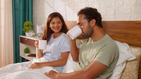 Happy relaxed indian couples drinking coffee or tea after wake up on bedroom - Stock Footage 266534130