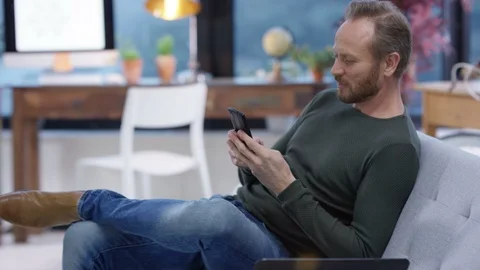 Happy relaxed man using mobile phone on sofa in living room Stock Footage 106794548