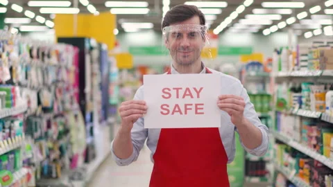 Happy retail worker in red apron wearing plastic face shield standing in Stock Footage 148104388