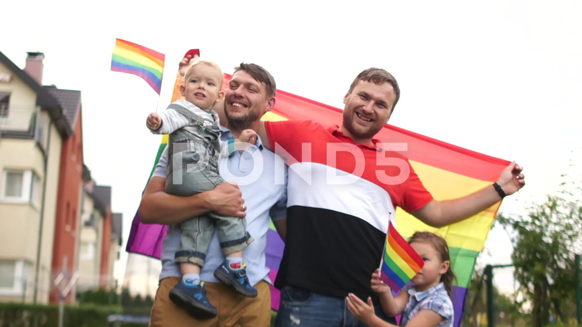 Happy same-sex family near their house with flags and two children, a boy  and a