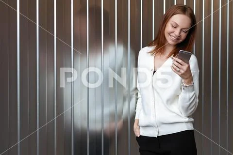 Happy satisfied browses website on cell phone, wears white jumper and black t Stock Photos
