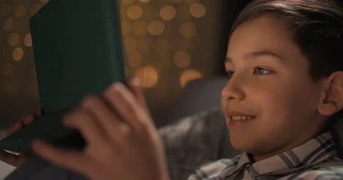 Happy schoolboy smiling while sitting on sofa watching at the tablet at night Stock Footage 243094786