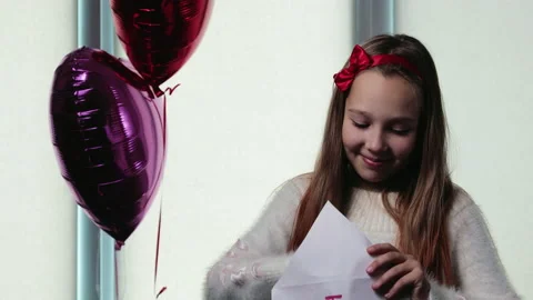 Happy schoolgirl takes out a valentine card from the envelope on the background Stock Footage