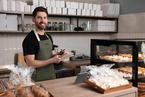 Happy seller with notebook and pen at cashier desk in bakery shop Stock Photos