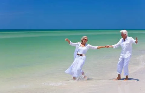 Happy senior couple dancing holding hands on a tropical beach Stock Photos