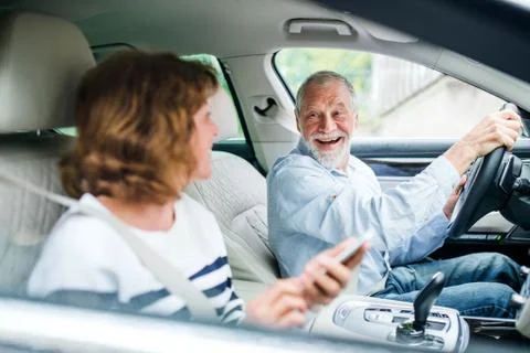 Happy senior couple with smartphone sitting in car, going on trip. Stock Photos