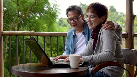 Happy senior couple using laptop computer at home with green garden background . Stock Footage 129583928