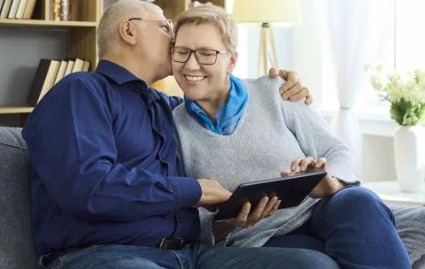 Happy senior couple using tablet at home, sharing affection and learning Stock Photos