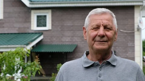 Happy senior elderly man looking at camera, outdoors, house on background Stock Footage 132887396