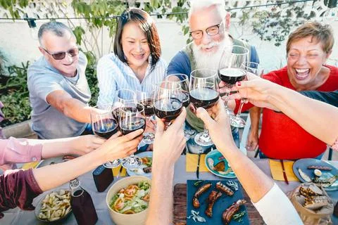 Happy senior friends toasting with red wine glasses at dinner time outdoor Stock Photos