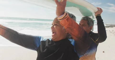 Happy senior hispanic couple walking on beach with surfboard over heads Stock Footage 340963833