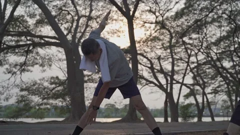Happy senior man exercise and stretching at lake park under tree in evening suns Stock Footage 157983159