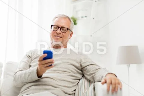 Happy senior man texting on smartphone at home Stock Photos