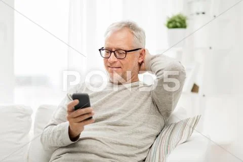 Happy senior man texting on smartphone at home Stock Photos