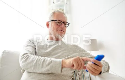 Happy senior man texting on smartphone at home Stock Photos