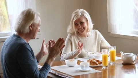Happy senior older couple talking laughing having healthy morning breakfast Stock Footage