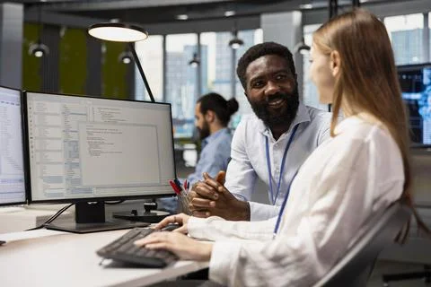 Happy senior programmer mentoring junior developer at desk in office Stock Photos