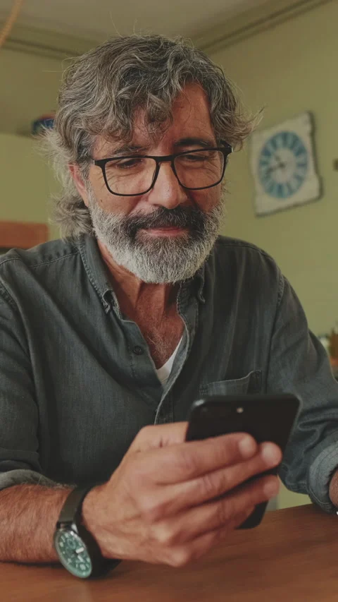 Happy senior reading message on his smartphone and drinking coffee while sitting Stock Footage 229507799