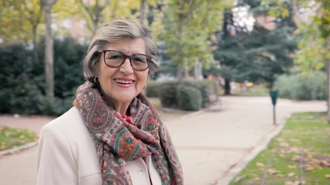 Happy senior woman in a park smiling to camera. Dolly in, slow motion Stock Footage