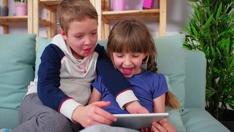 Happy siblings lying on sofa at home and playing with pc tablet together Stock Footage 73511571