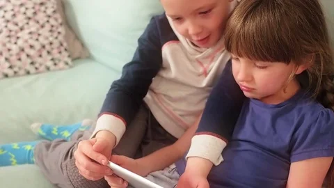 Happy siblings lying on sofa at home and playing with pc tablet together Stock Footage 73512207