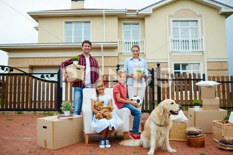 Happy siblings sitting in the yard by packed things with parents on background Stock Photos