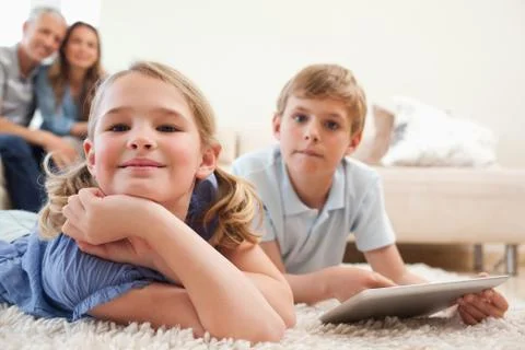 Happy siblings using a tablet computer with their parents on the background 写真素材
