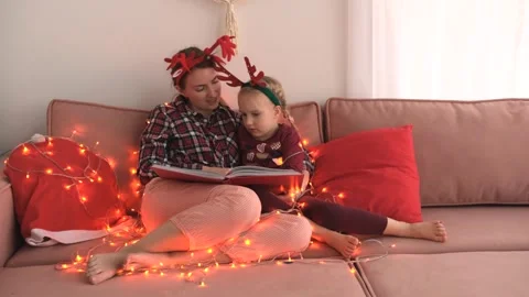 Happy single parent mom and daughter wearing fun headbands reading book on sofa Stock Footage 258374041