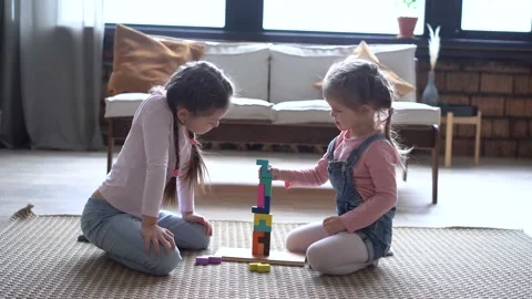 Happy sisters sitting on carpet, playing with colorful wooden blocks constructor Stock Footage 147388257