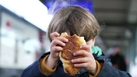 Happy small boy eating croissant standing at train platform wearing jacket .. Stock Footage 252948558