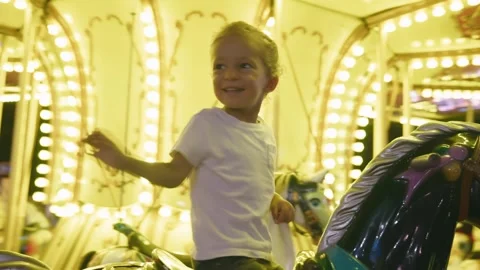 Happy small boy riding carousel at park, kid enjoying summer night seated on top Stock Footage 253849197