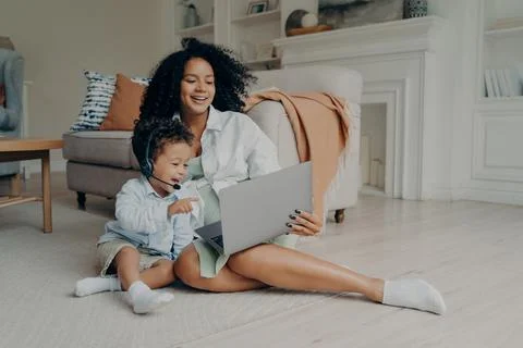 Happy small kid boy using headset while talking online on laptop, sitting on Stock Photos