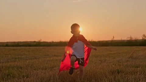 Happy smiling blond boy in red hero cloak runs through meadow field in rays of Stock Footage 158052712