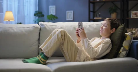 Happy smiling boy relax at home in the evening, using mobile phone, browsing Stock Footage 265609603