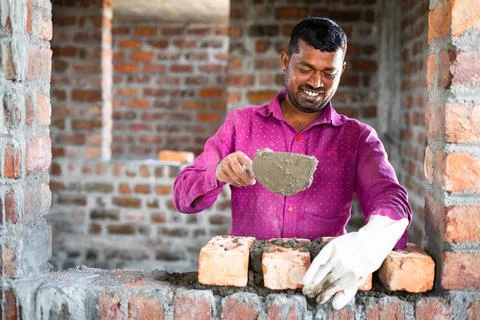 Happy smiling construction worker constructing or building wall by placing Fotos de archivo