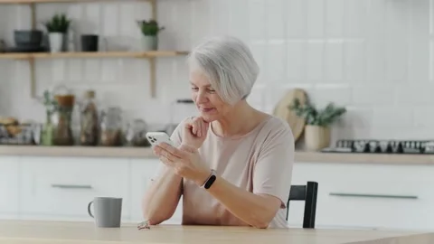Happy smiling elderly woman using phone, looking at screen, sitting in living Stock Footage 237961259