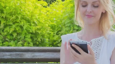 Happy smiling girl using a smart phone in a city park  Stock Footage 64699229