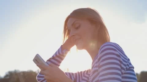 Happy Smiling Girl Using SmartPhone in City Park Sitting on the Bench at sunset Stock Footage 67437448