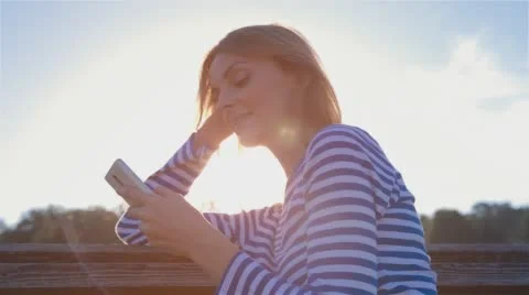 Happy Smiling Girl Using SmartPhone in City Park Sitting on the Bench at sunset Stock Footage 67437573