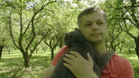 Happy smiling handsome man Stroking a Cat and walks through green trees alley. Stock Footage 110778485